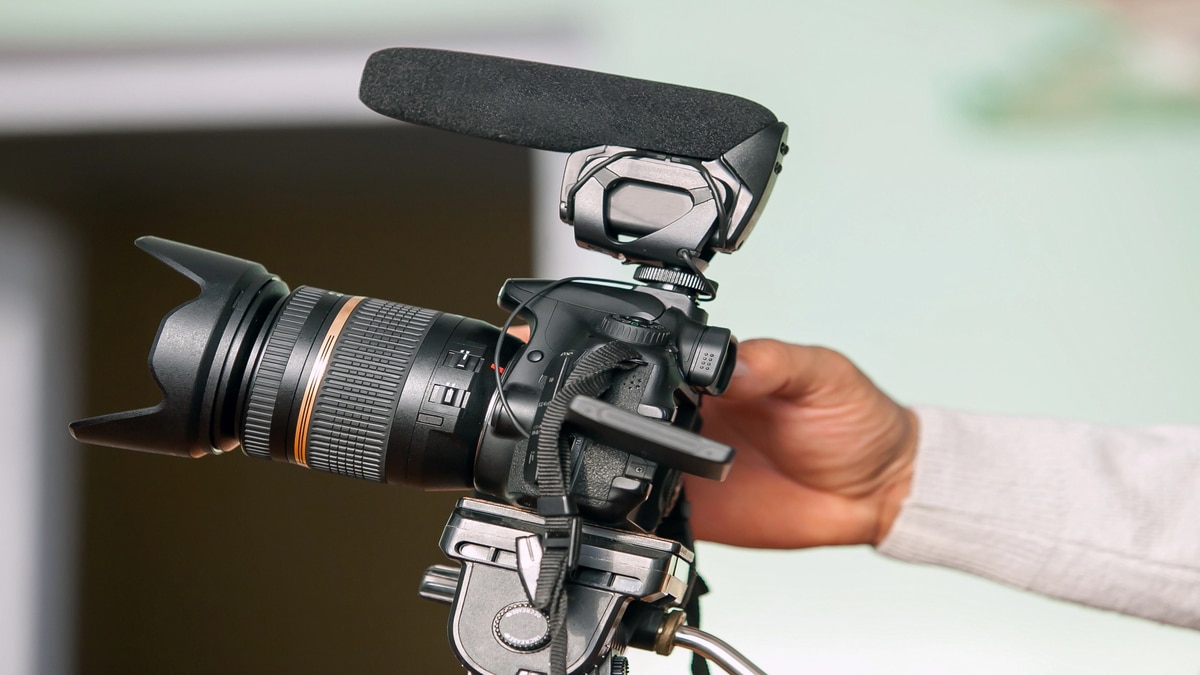 Capture on a Tight Budget: 5 Ways to Reduce Cost Without Losing Quality Close-up of a DSLR camera with an external microphone mounted on top, held by a person’s hand, ready for video recording.
