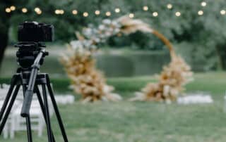Wedding videography setup with camera on tripod capturing outdoor ceremony arch.