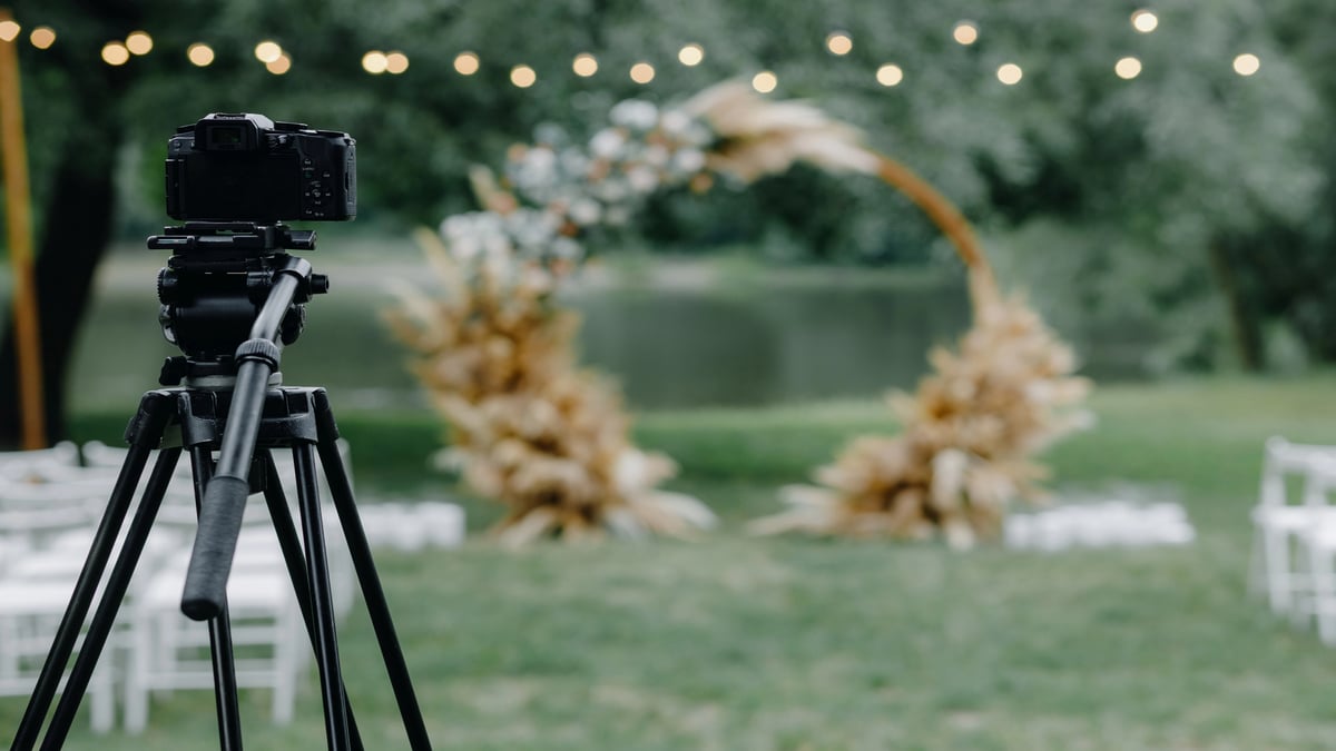 Wedding Videography vs. Photography: What Moments Video Captures That Photos Miss Wedding videography setup with camera on tripod capturing outdoor ceremony arch.